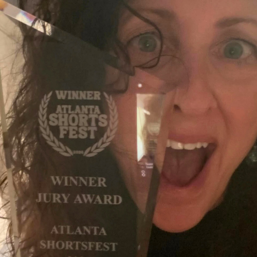 Woman holding a trophy that reads 'Winner Atlanta Shorts Fest Winner Jury Award' with her mouth open in excitement.