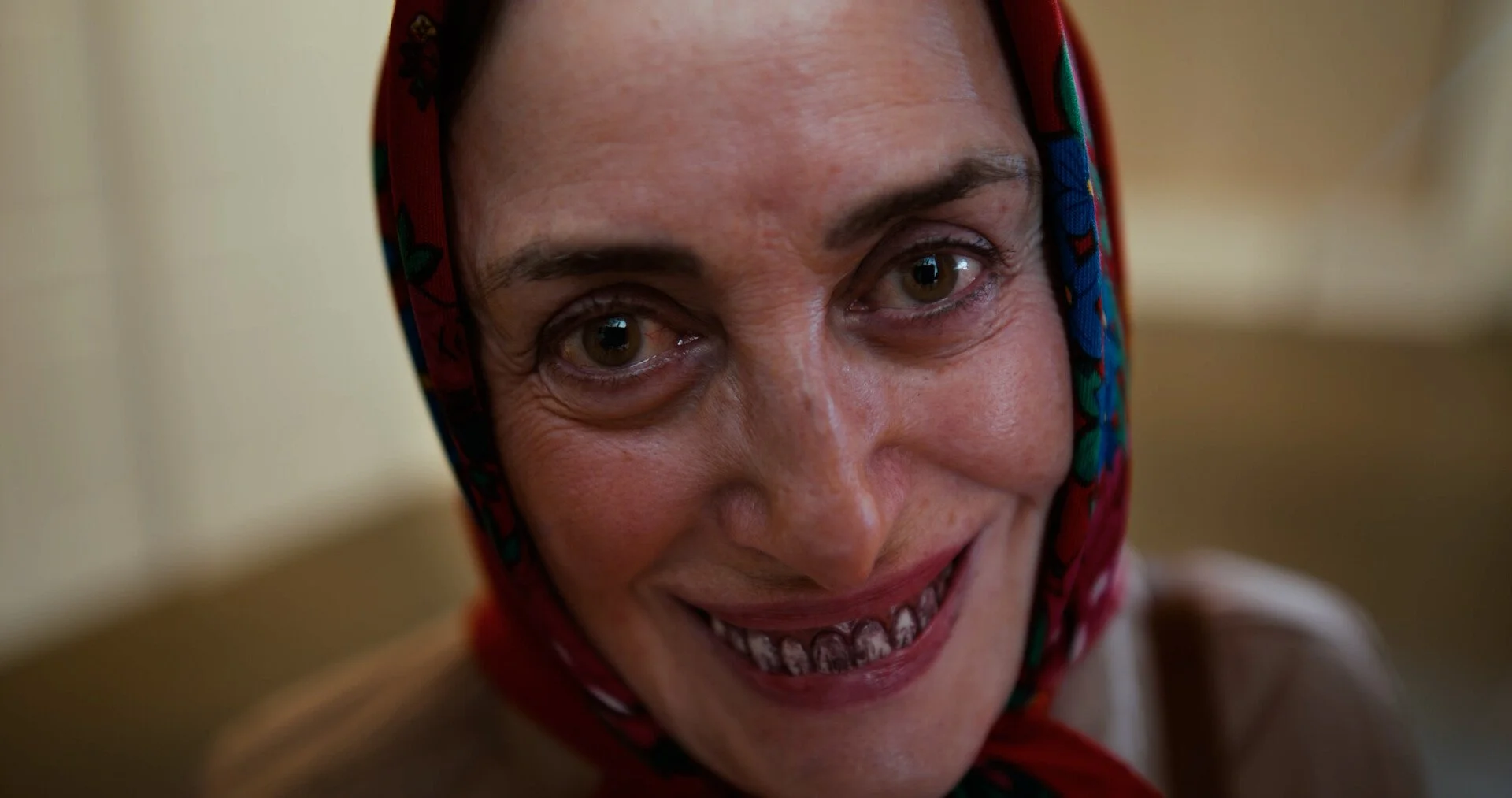Close-up of a woman with a colorful scarf smiling, with a bright expression and visible teeth.