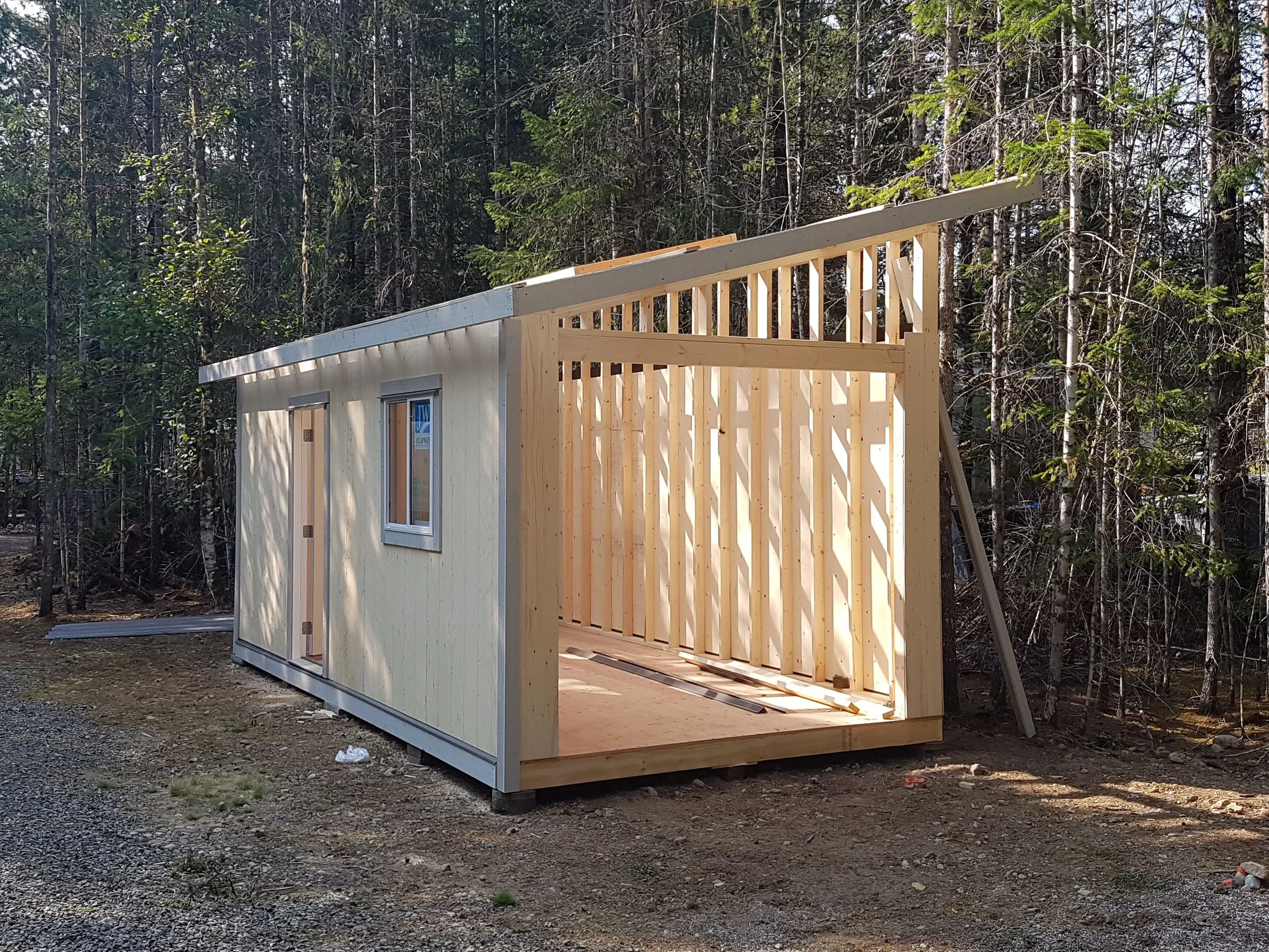 Partial view of a house under construction with wood framing, set against a wooded forest background.