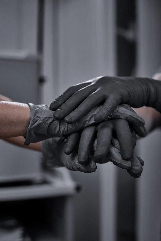 Two people wearing black disposable gloves shake hands.