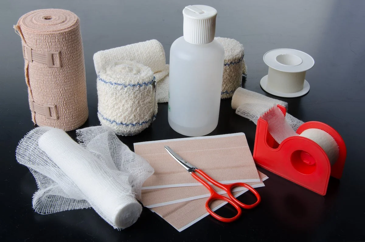 Medical supplies including gauze rolls, tape, scissors, tape dispenser, spray bottle, and bandage pads.
