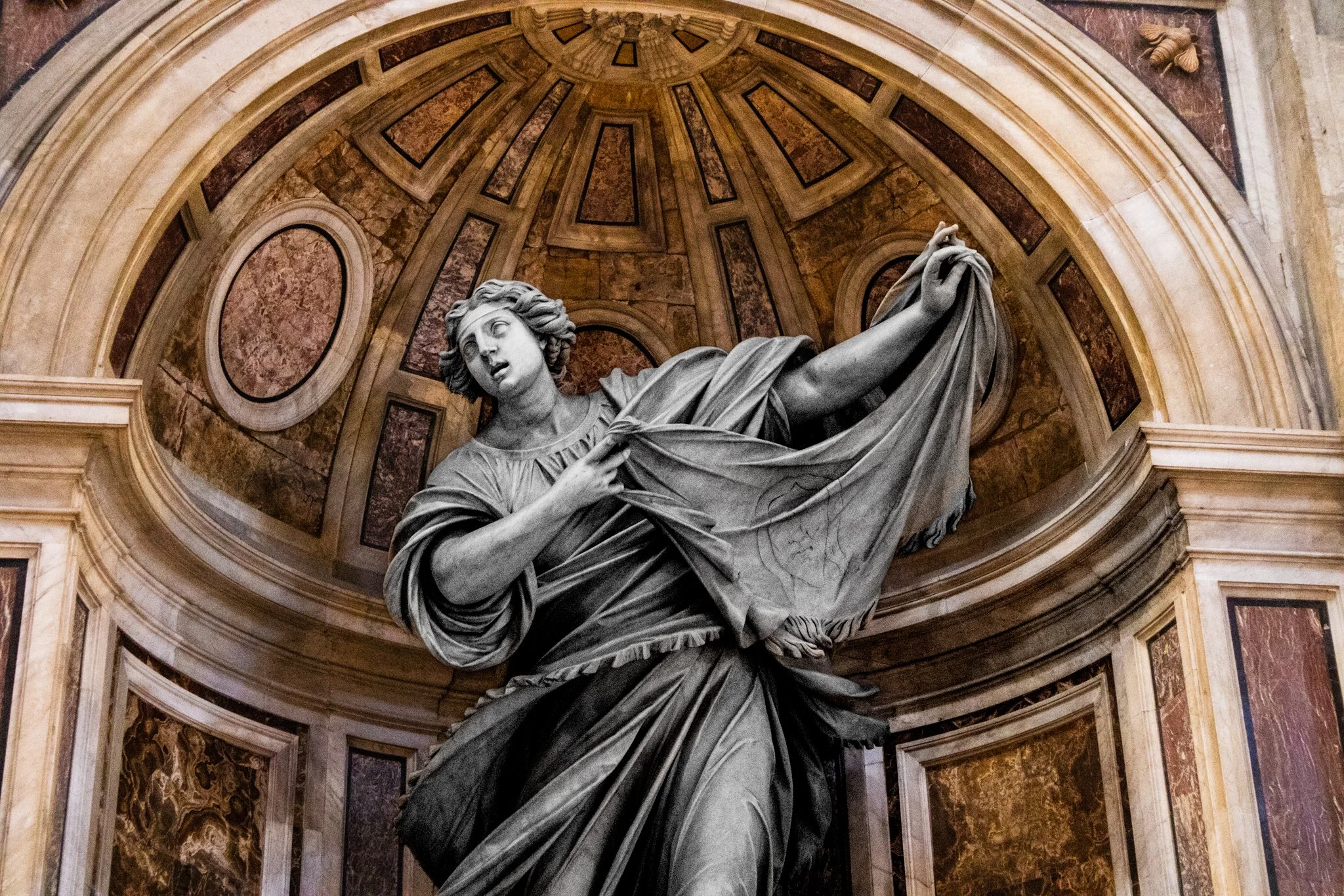 Statue of a woman holding a sword or sword-like object, situated in a domed interior with ornate marble and gold accents.