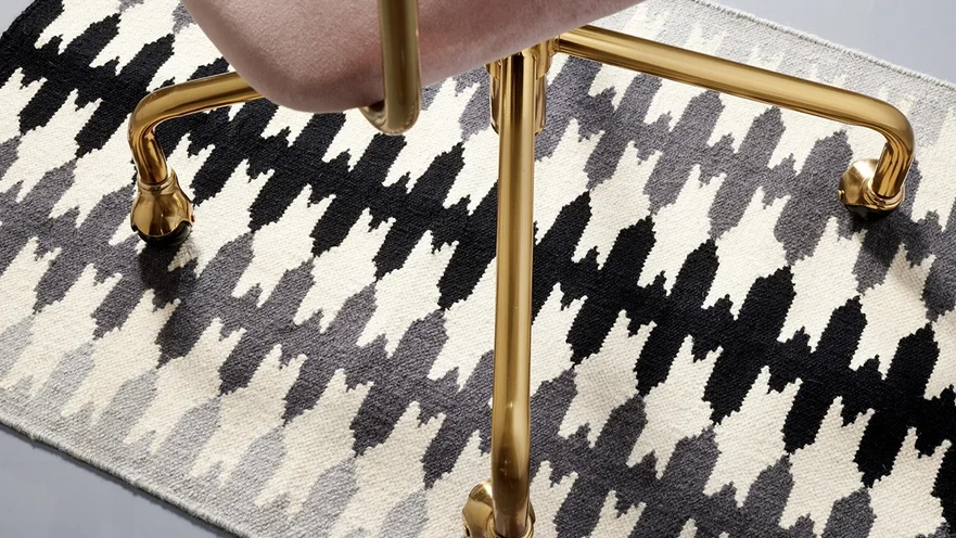 Close-up of a chair with gold metal legs on a black and white houndstooth patterned rug.