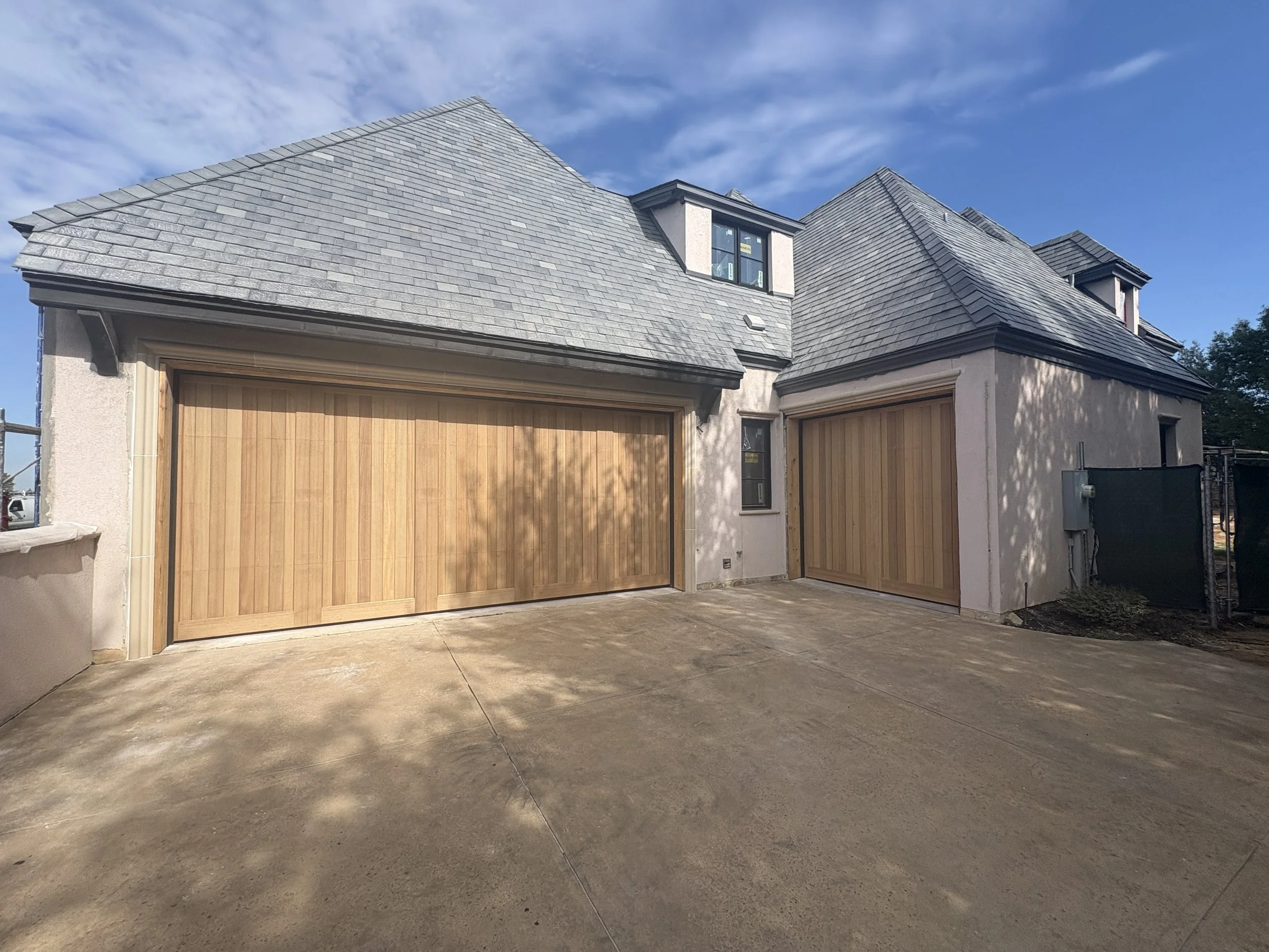 A residential house with a slate roof, wooden garage doors, and a concrete driveway.