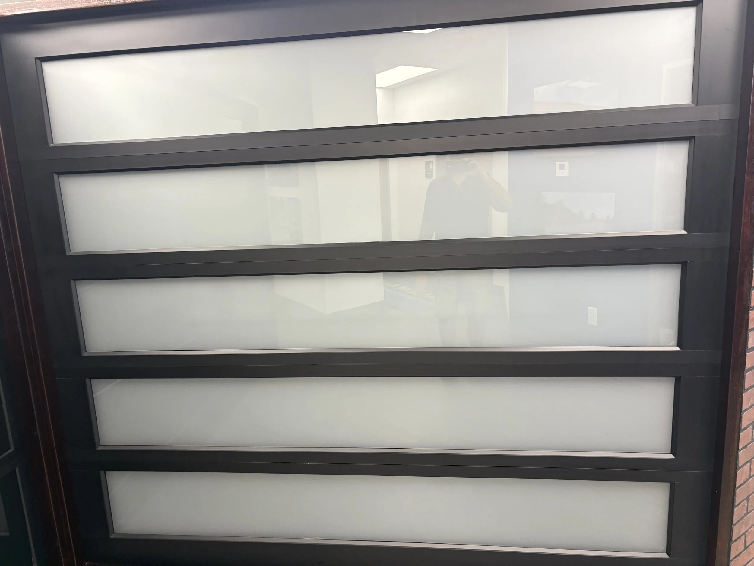 A sectional view of a modern glass door with multiple frosted glass panels and a black metal frame.