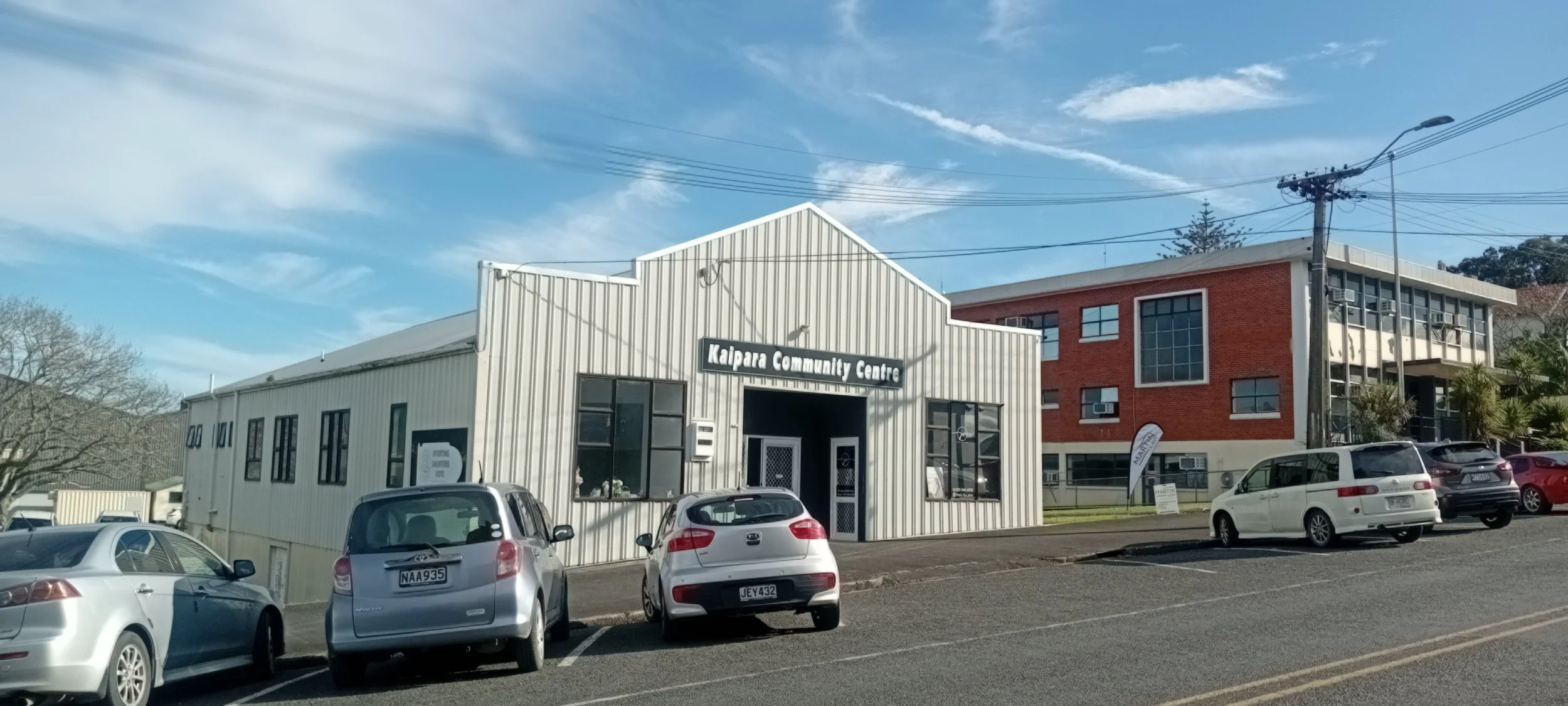 Kaipara Community Centre building with parked cars in front under a blue sky.