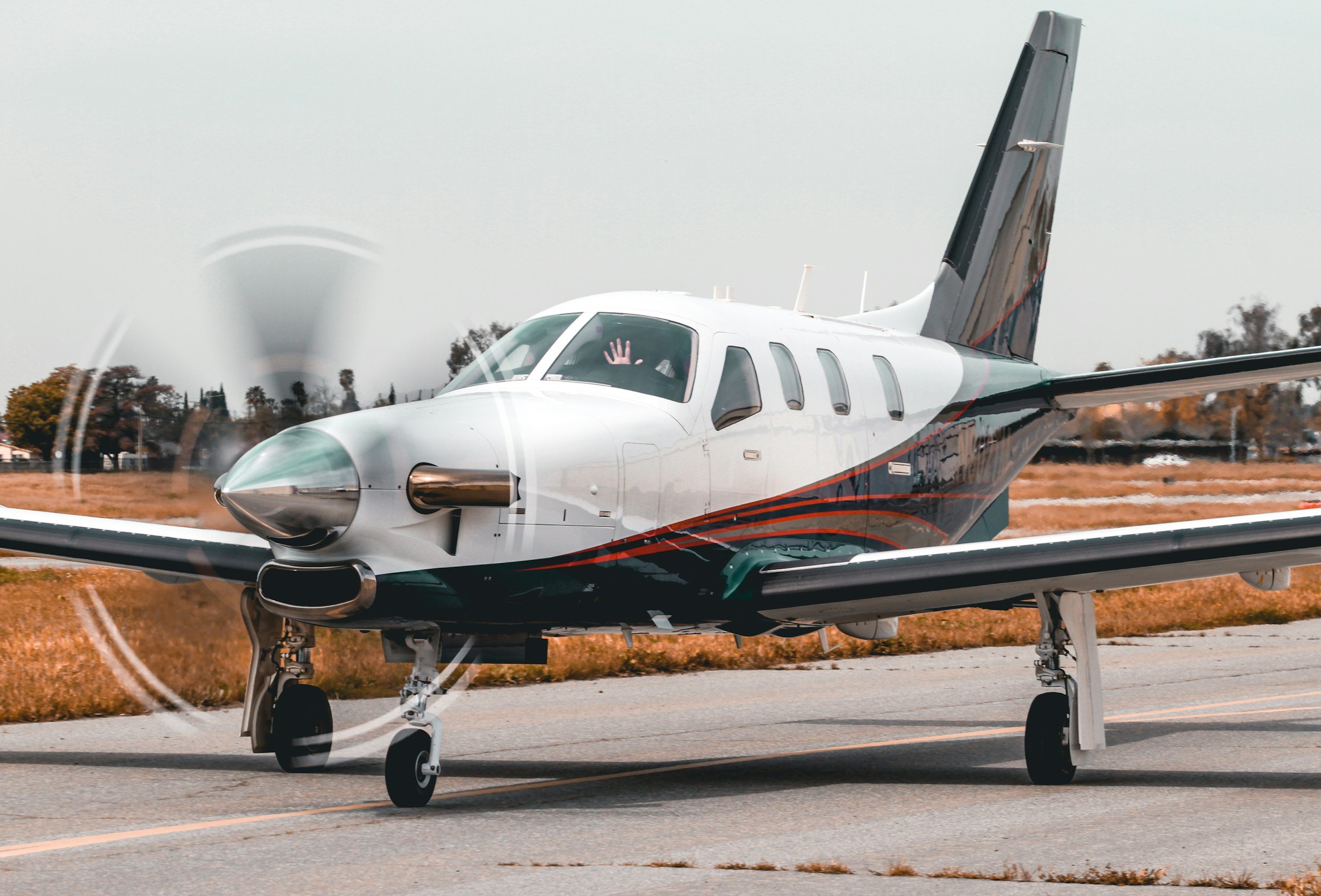 A modern private jet airplane on the runway, with a hand waving from the cockpit window.