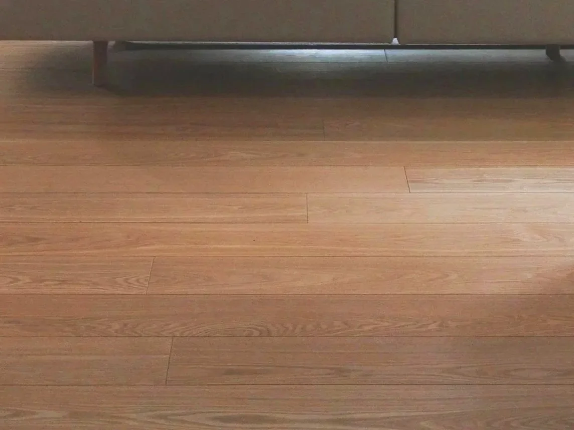 View of a hardwood floor with the bottom part of a sofa visible at the top of the image.