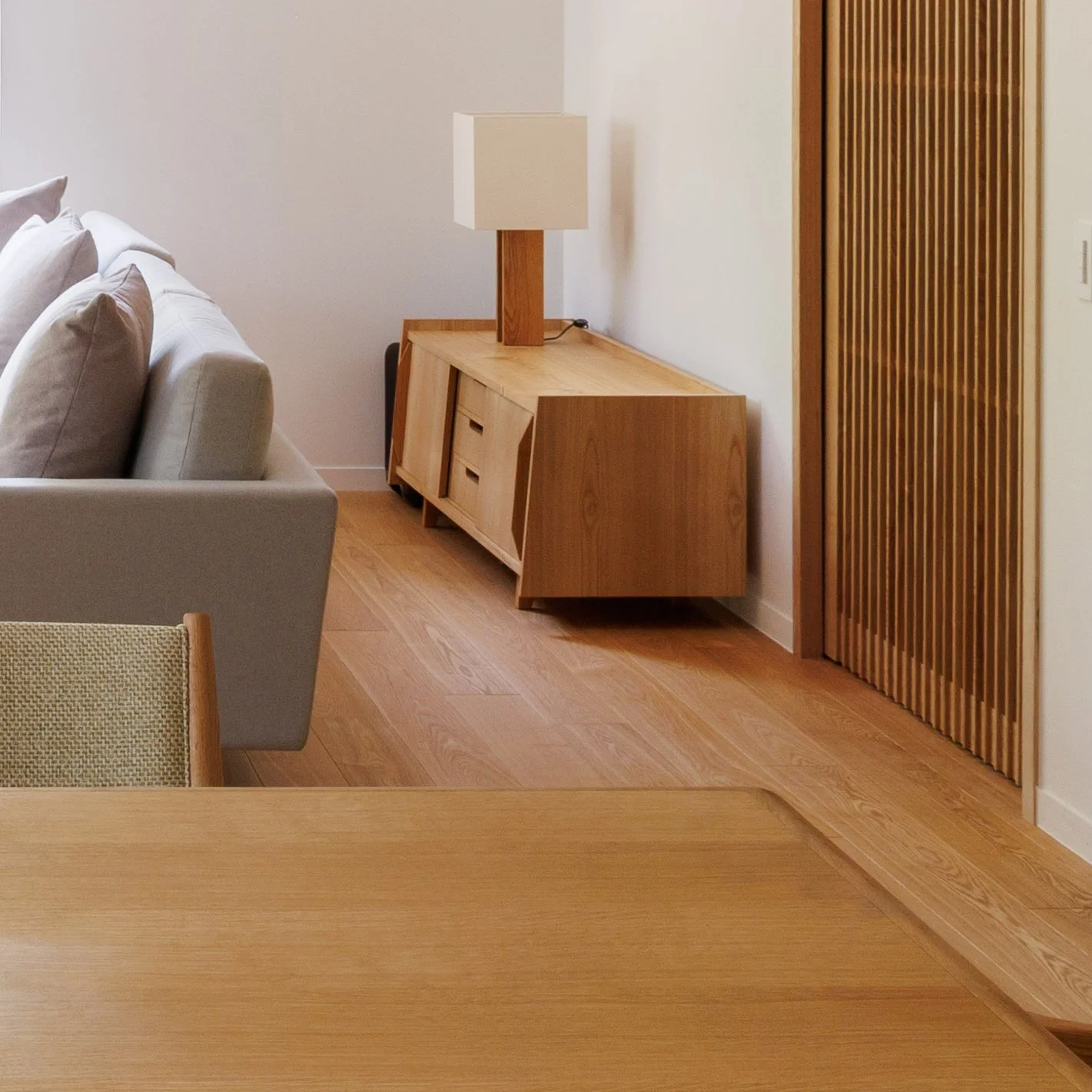 Living room corner with a beige sofa, wooden sideboard, and lamp, with a wooden door on the right.