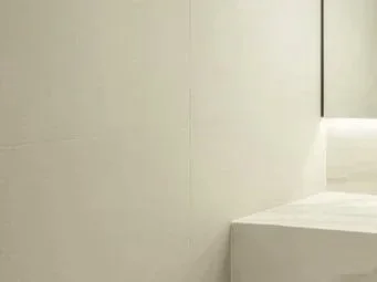 Part of a minimalistic bedroom with a white bed and light-colored walls.