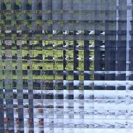 A distorted and pixelated image of a road with a vehicle and some greenery, seen through a glass window with a grid pattern.