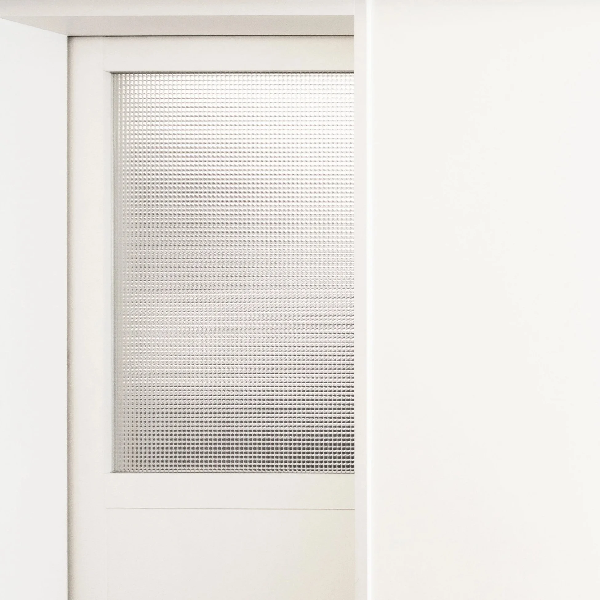 Close-up of a white air vent panel with a perforated metal grille, set into a white wall.