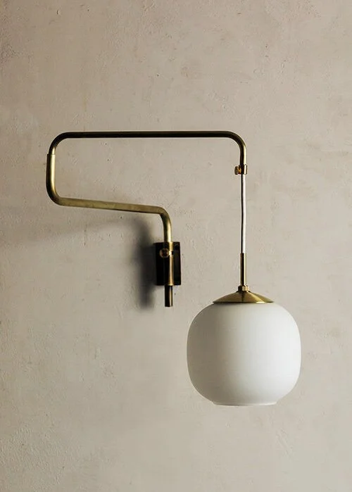 Wall-mounted lamp with a curved brass arm and a white spherical shade