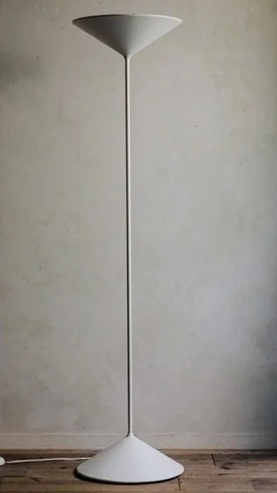White modern floor lamp with a conical top and rounded base against a plain wall.