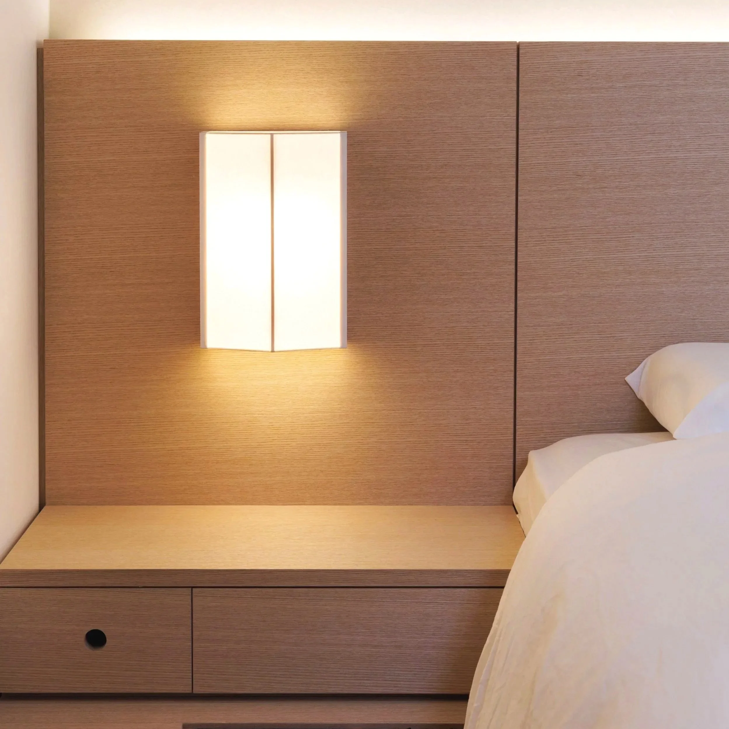 A wooden headboard with a built-in rectangular light fixture and a bed with white pillows partially visible on the right side.