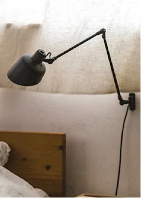 Black adjustable wall-mounted lamp on a white wall above a wooden headboard.