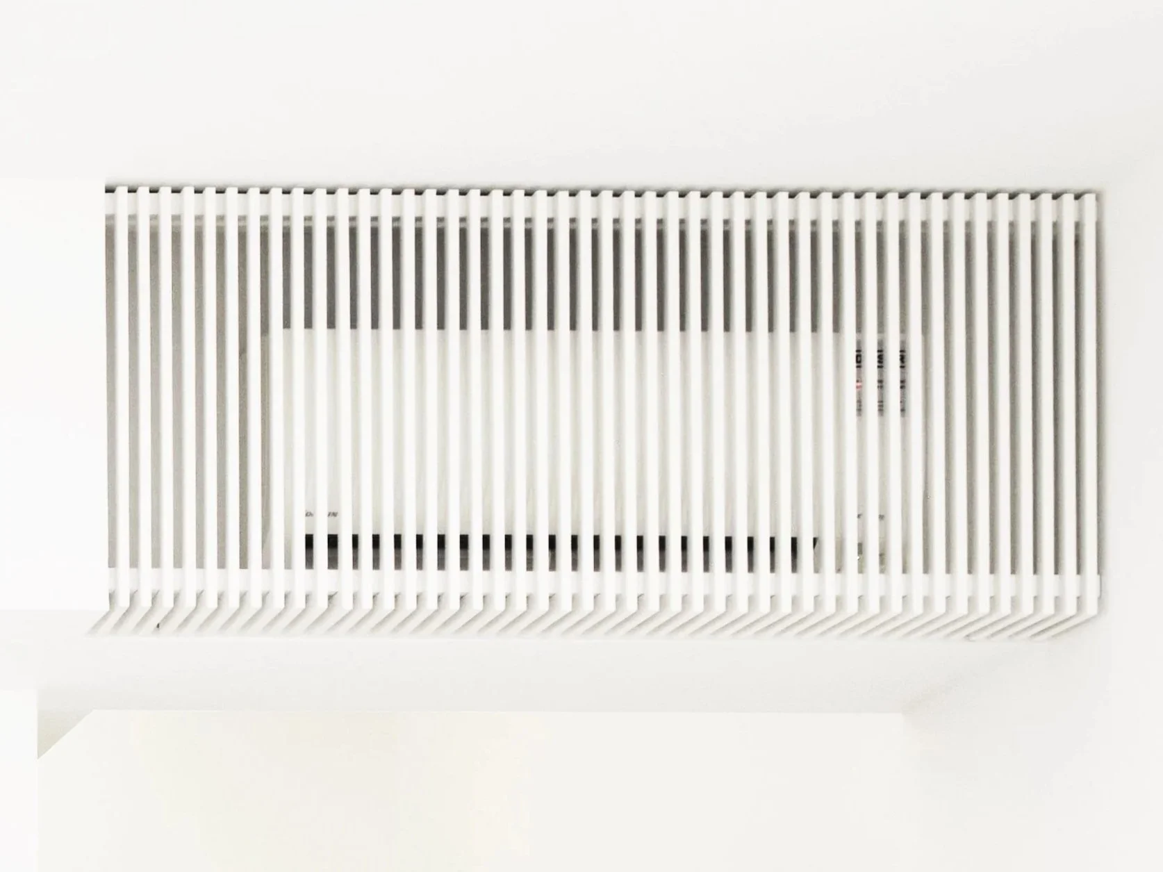 White air vent or radiator cover on a white wall with a rectangular shape and vertical slats.