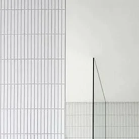 Close-up of a modern building's exterior with vertical and horizontal metal lines and a thin antenna against a plain white wall.