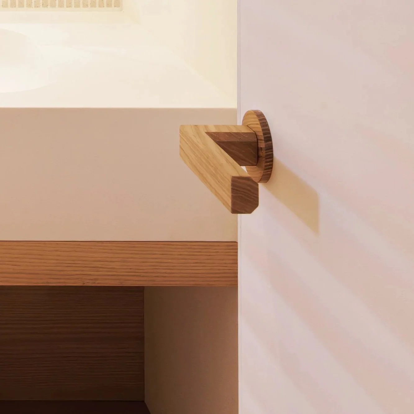 A wooden wall hook shaped like a house with a circular base, mounted on a white wall.