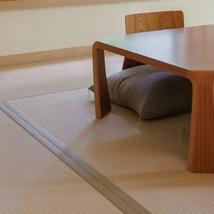 A low wooden table with rounded edges sits on a tatami mat, with a gray cushion underneath.