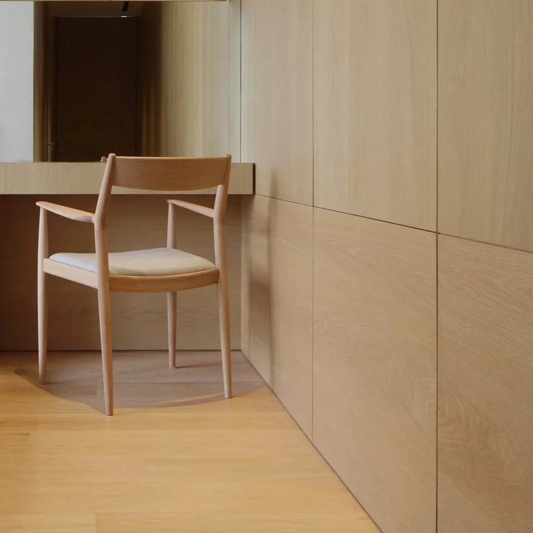 Wooden chair with a cushioned seat in a minimalistic room with light wood panel walls and flooring.