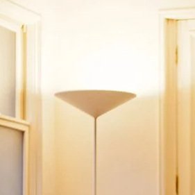 A tall floor lamp with a beige lampshade in a bright room with cream-colored walls.