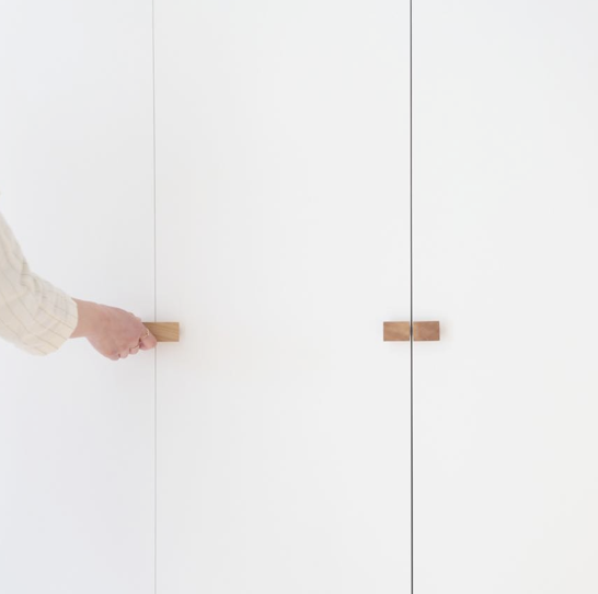 Person opening a white closet door with a wooden handle.
