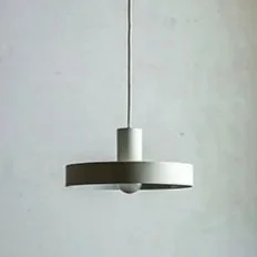 A modern, minimalist ceiling pendant light hanging from a wire against a plain wall.