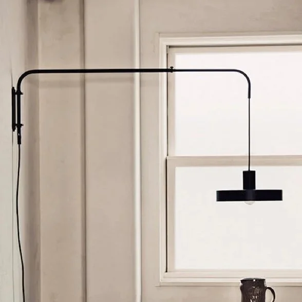 A black wall-mounted lamp with an adjustable arm in front of a window.