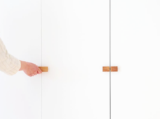 Person opening white closet doors with wooden handles.