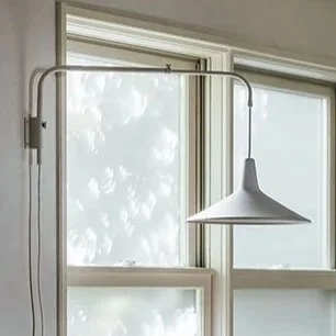 Close-up of a modern white pendant light hanging above a window with a sheer curtain, allowing natural light to enter the room.