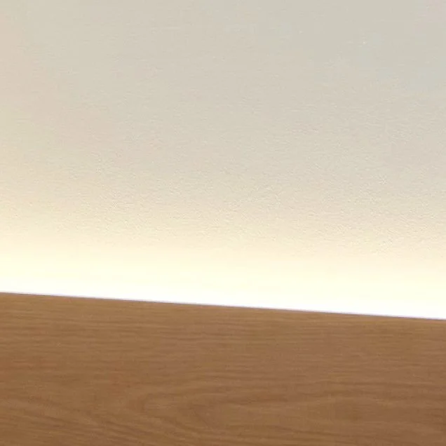 Close-up of a wooden surface with a beige wall in the background.