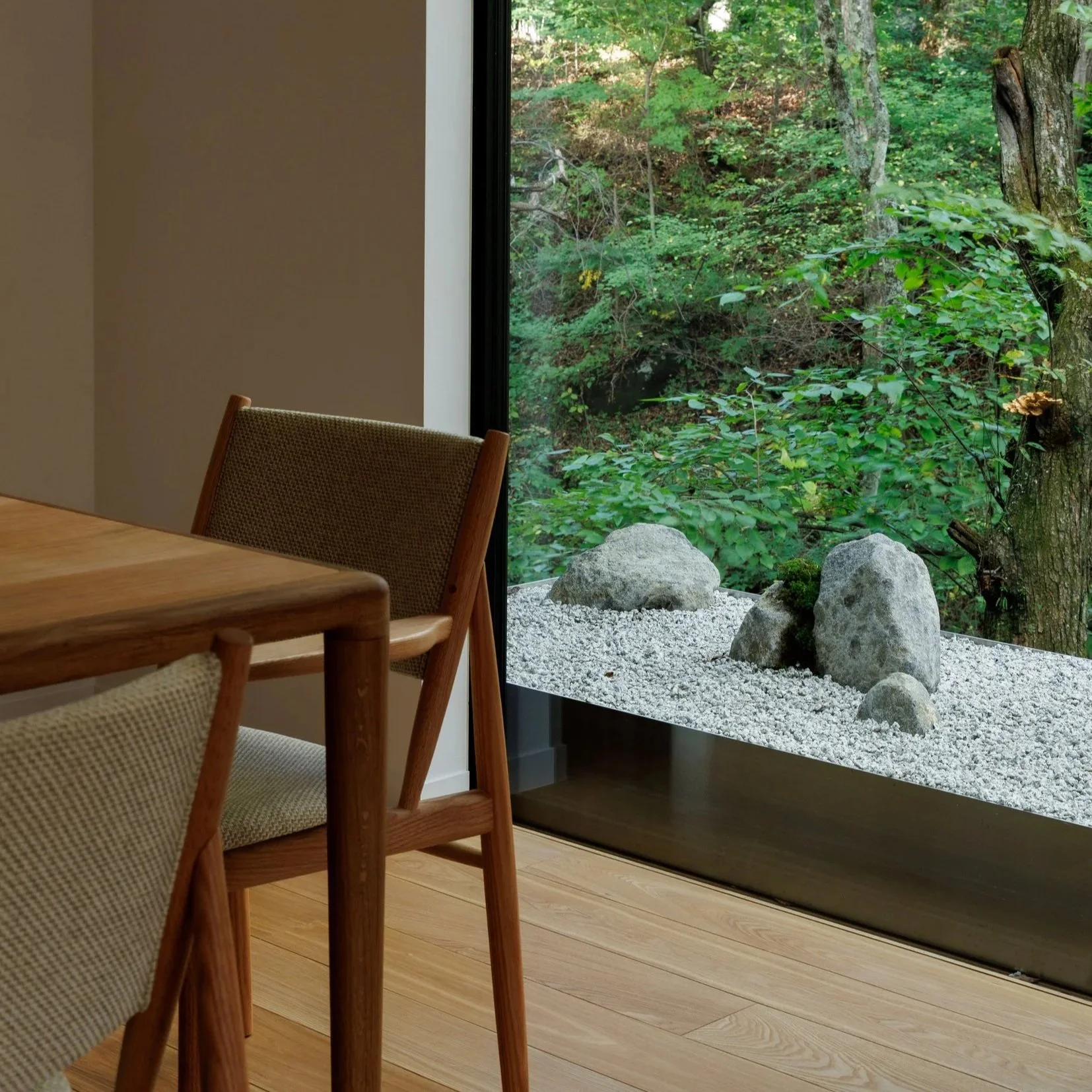 Interior of a room with a wooden table and chairs. Large window showing a Japanese rock garden with trees and rocks outside.