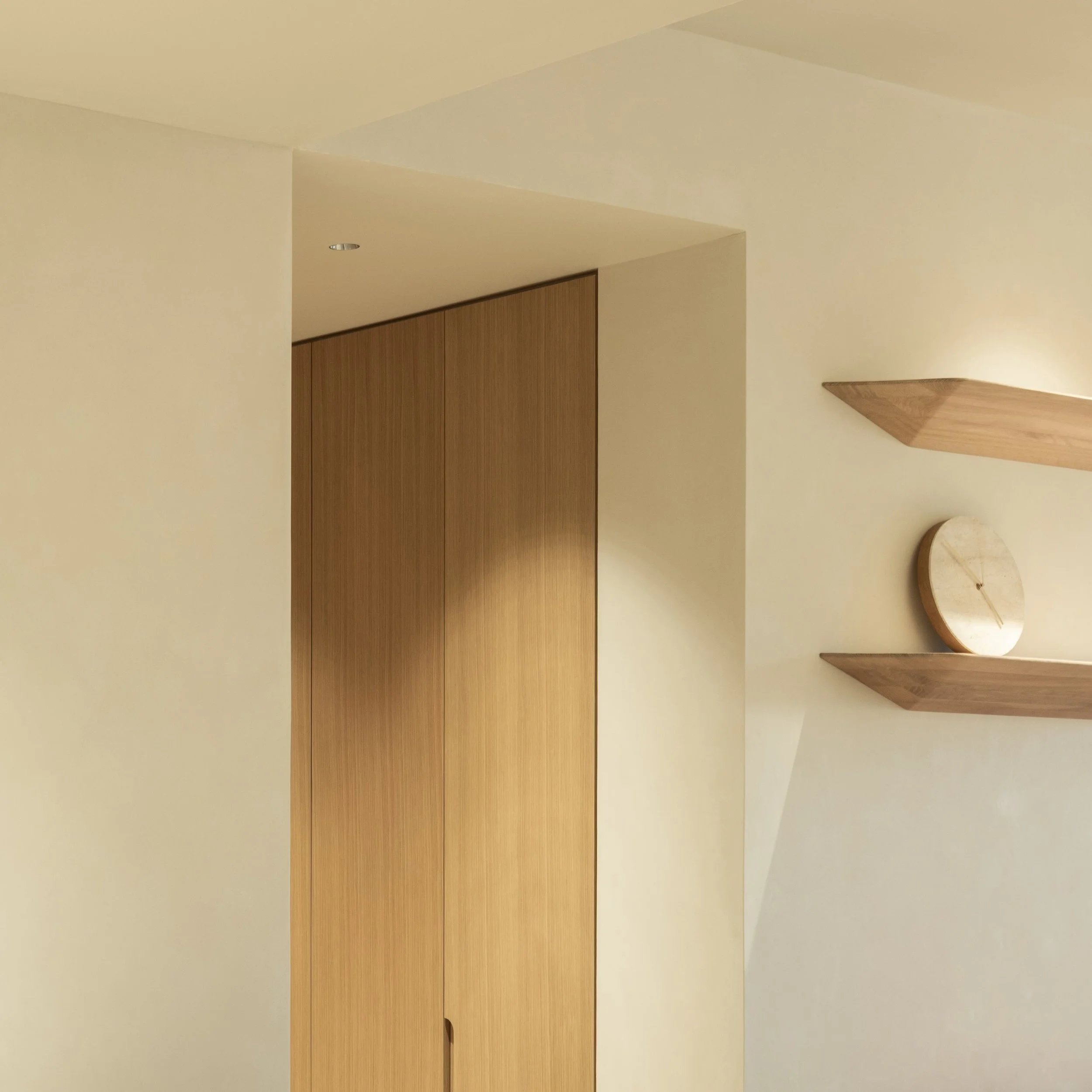 Interior of a room with cream-colored walls and a wooden ceiling element, with a wooden door or panel and a small circular table.