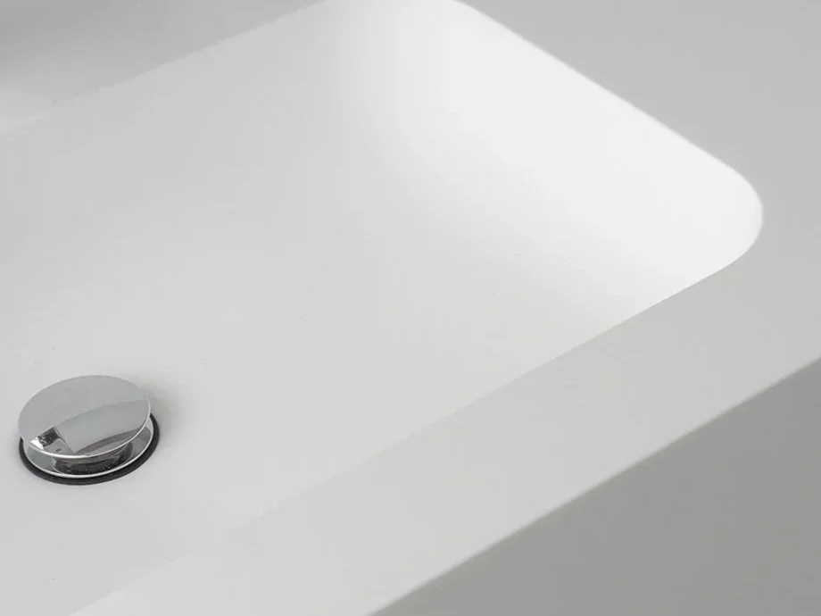 Close-up of a white sink with a shiny, round chrome drain stopper in the bottom left corner.