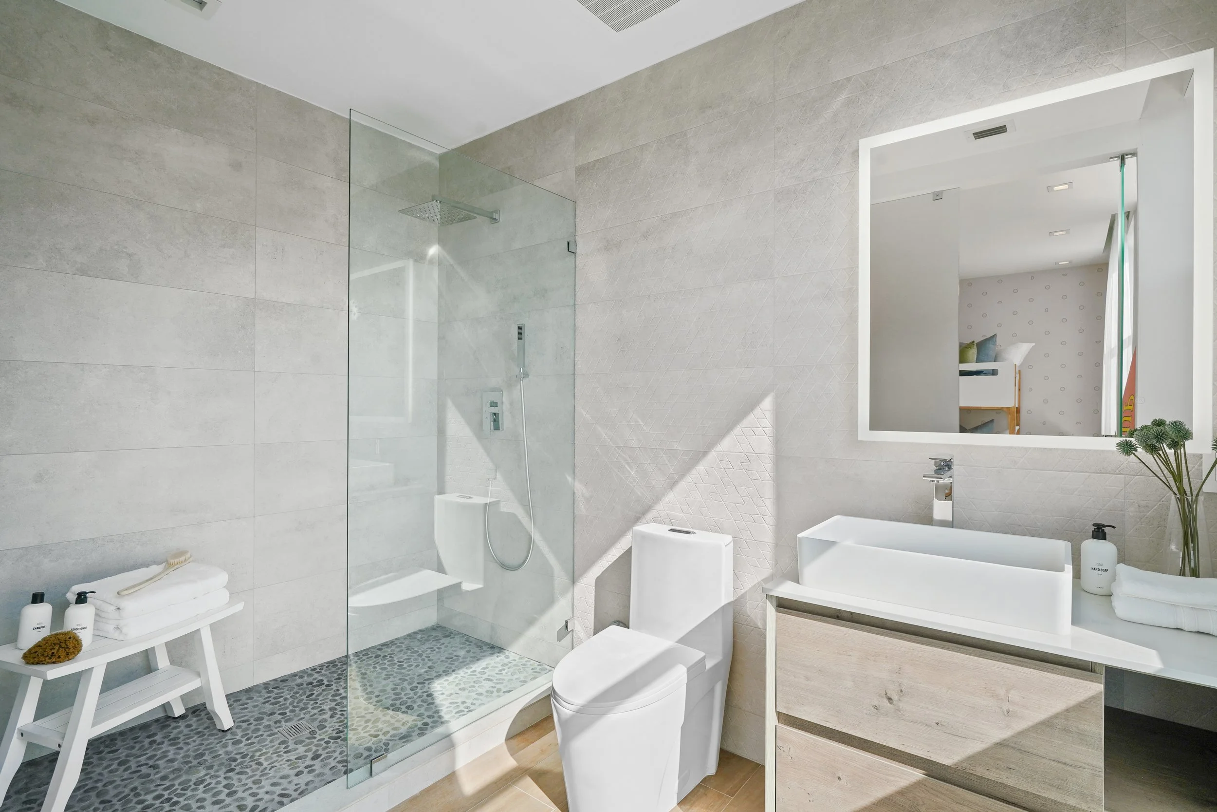 Modern bathroom with a walk-in shower, white toilet, vanity with mirror, and minimal decor including towels and bottles of soap or lotion.
