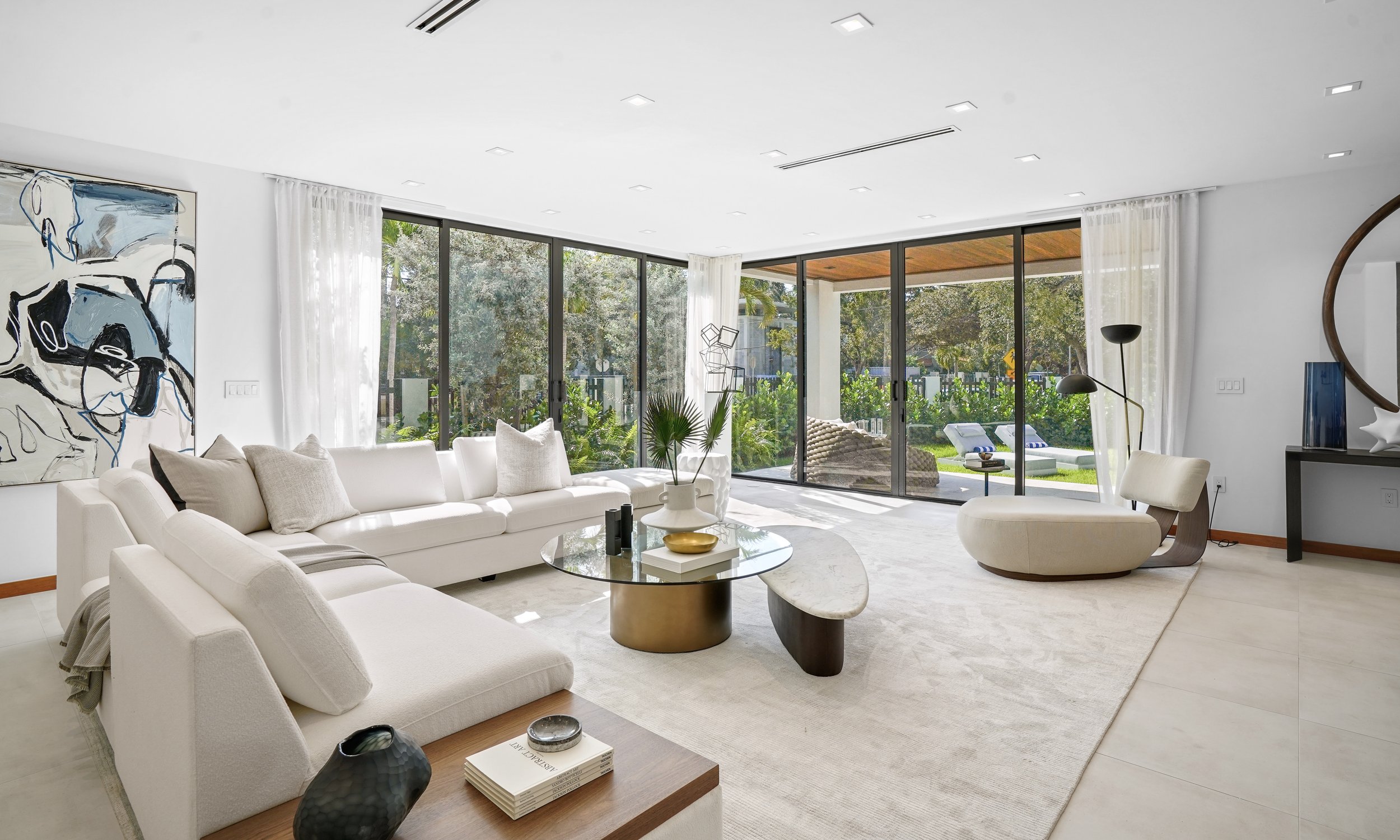 Modern living room with white sectional sofa, abstract wall art, glass sliding doors leading to outdoor patio, and minimalistic decor