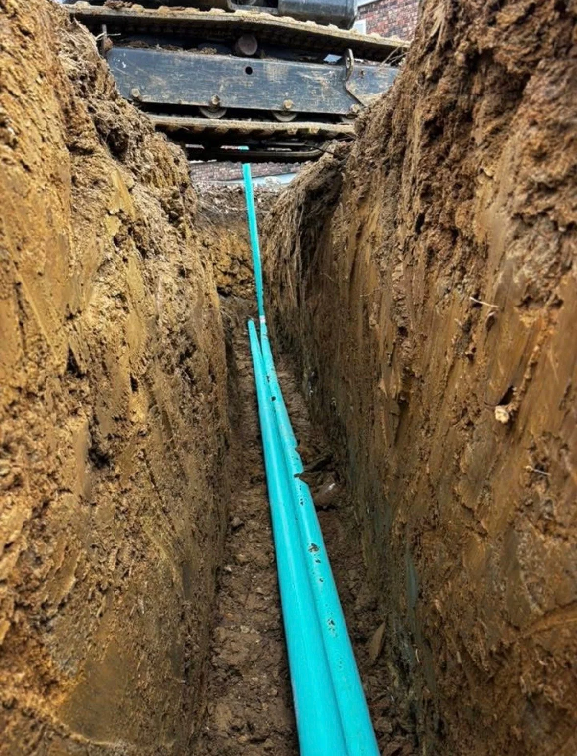 A photo of a narrow trench in the ground with blue pipes installed inside.