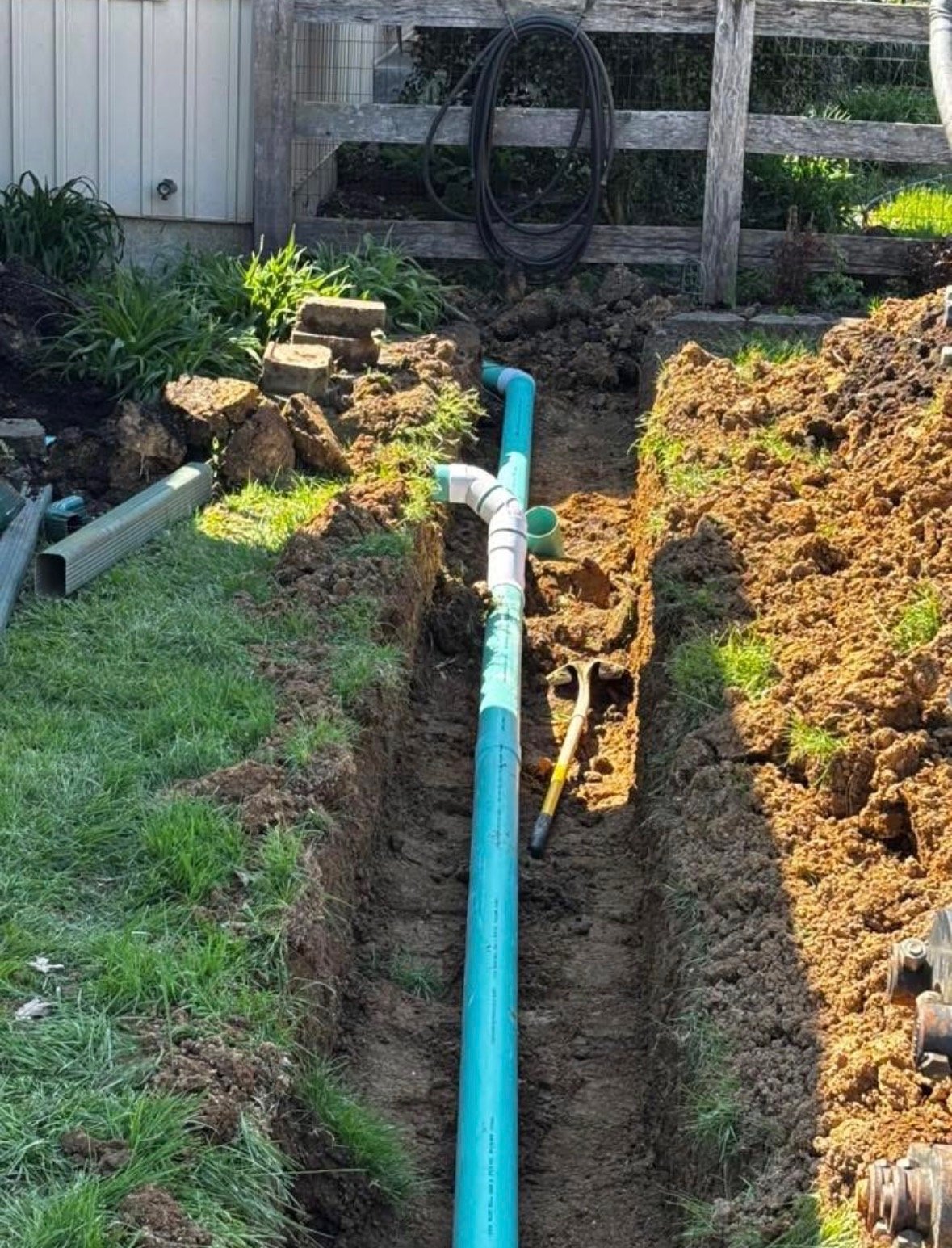 Underground plumbing installation with blue pipes in a trench in a backyard.