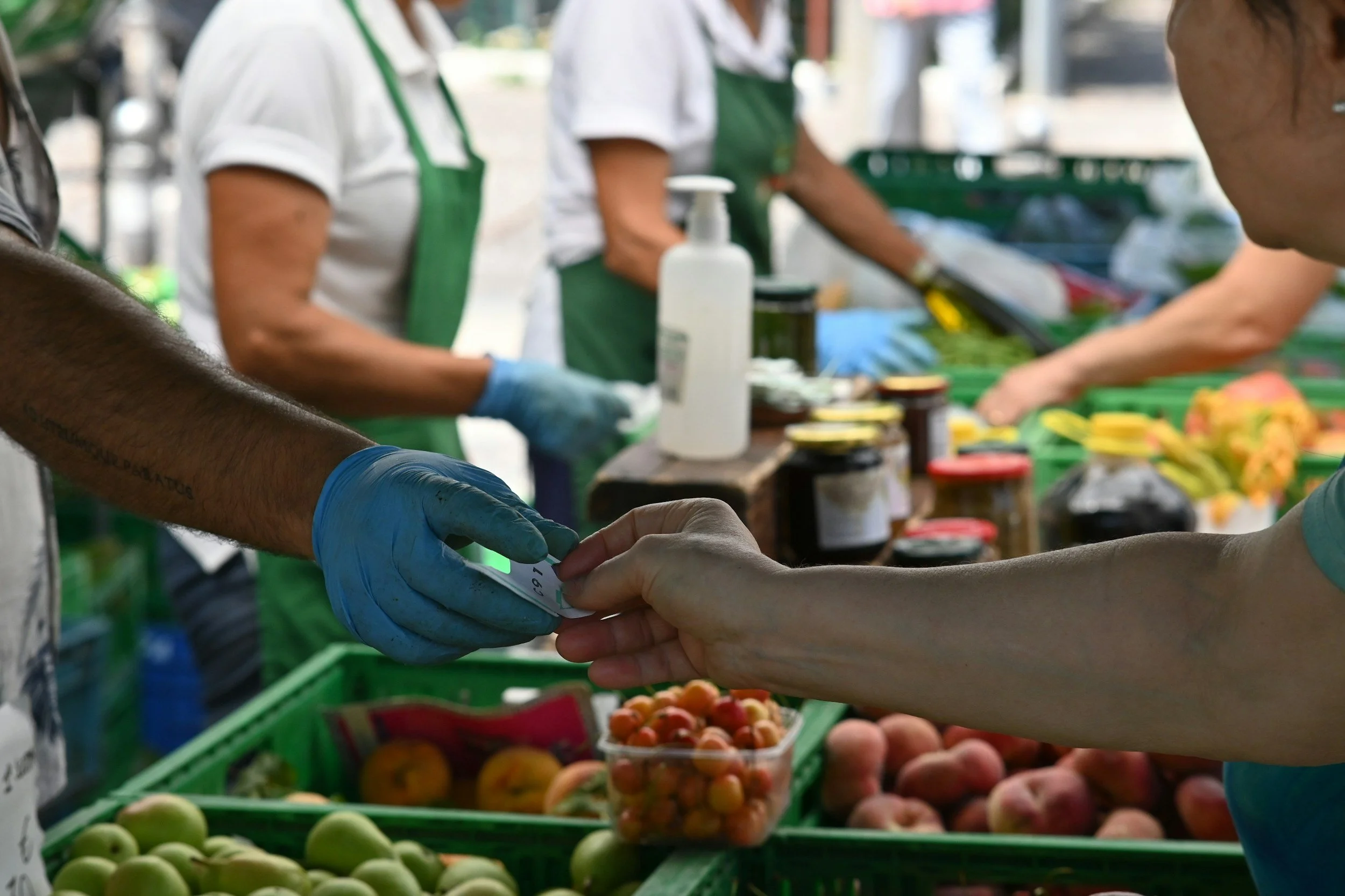 People at a farmers market exchanging money for produce, including peaches and apples.