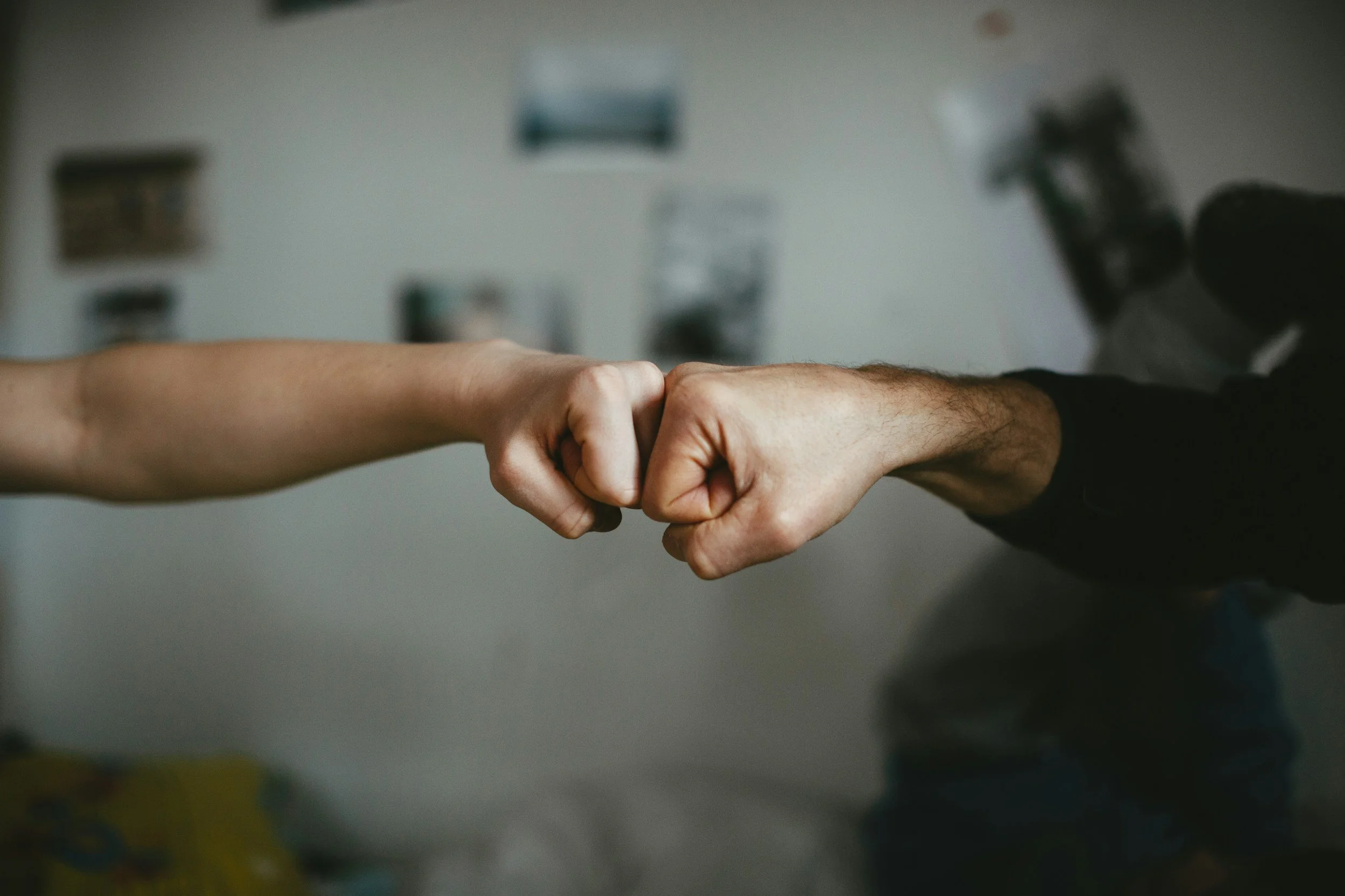 A close-up of two people engaging in a fist bump, with a blurred background.