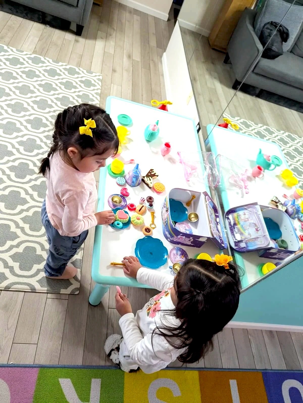 Young children with focused expressions leaning over a table examining a small animal inside a clear plastic habitat with a green lid, in a colorful classroom with storage bins and educational toys in the background.