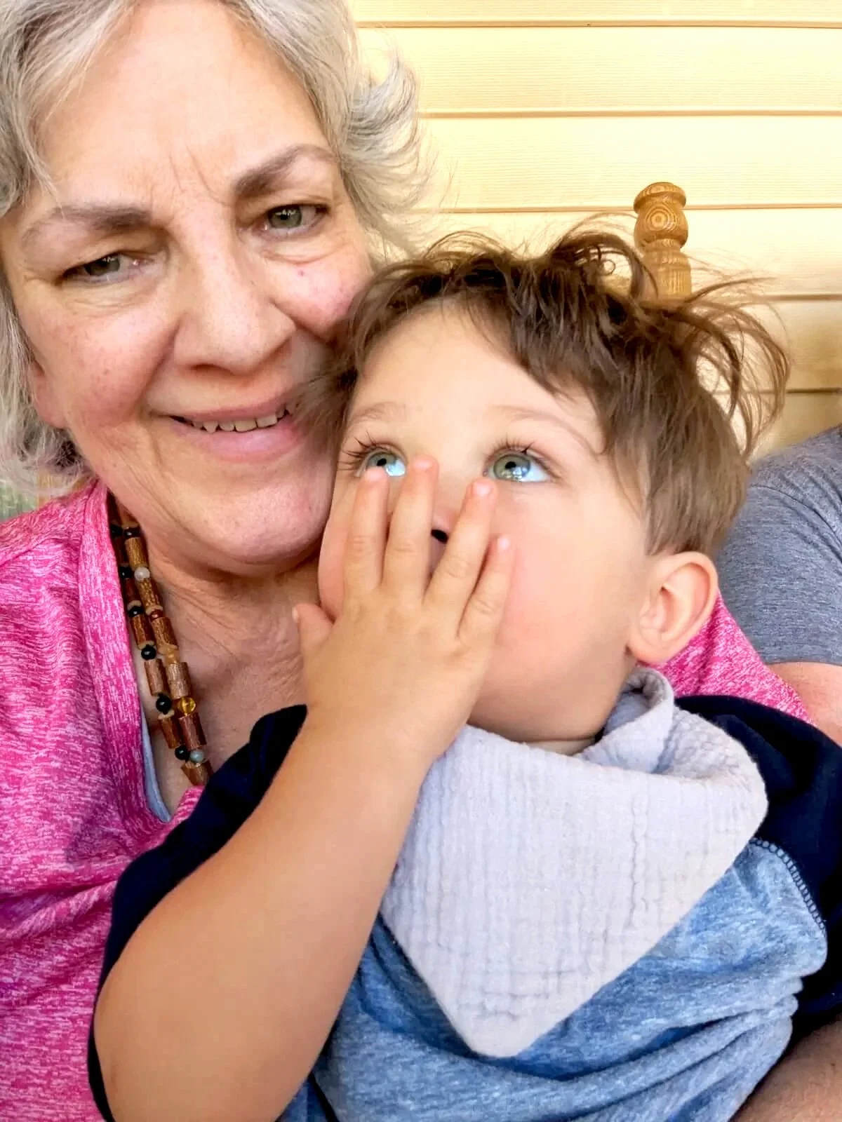 Carol and a young boy sharing a tender moment, with the woman smiling and the boy covering his mouth with his hand, both looking upward.
