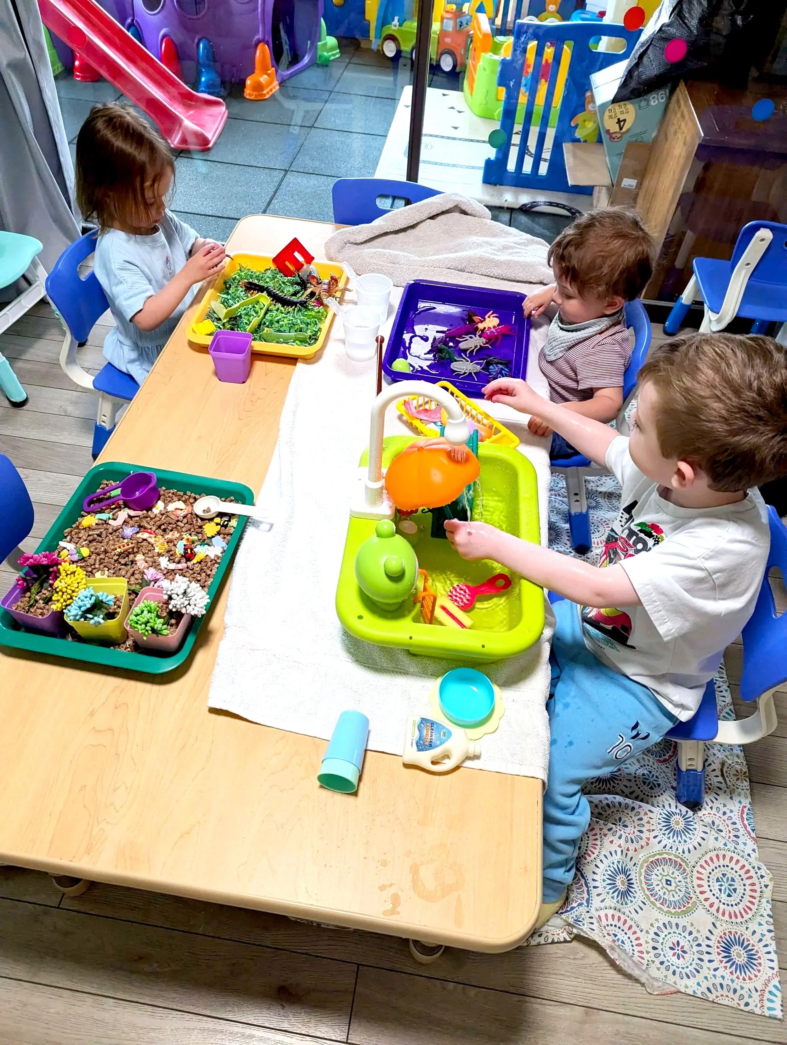 Children playing with colorful toy food and utensils at a play table in a playroom