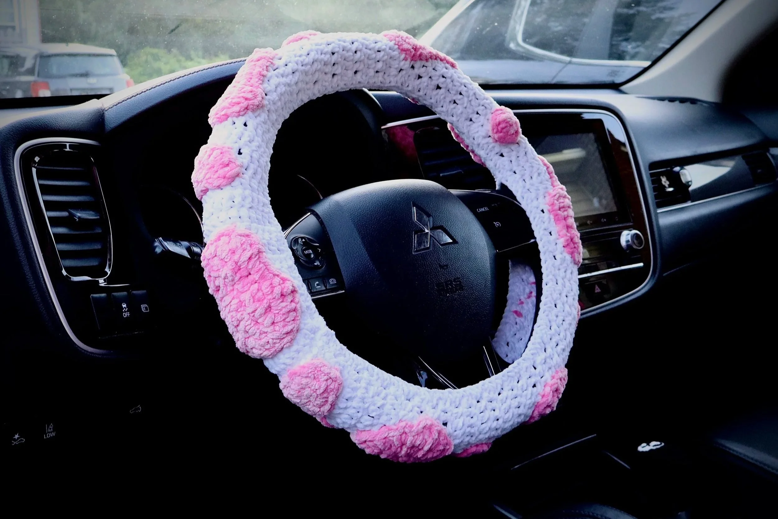 Photo of a Crochet Steering wheel cover with a pink spotted cow print, placed on a steering wheel.