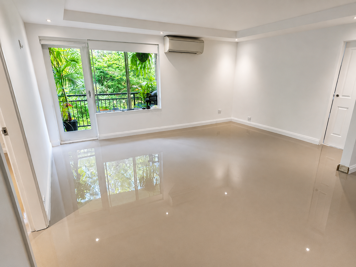 Empty bright room with large window and balcony door, white walls, glossy beige floor, air conditioner, and greenery outside.