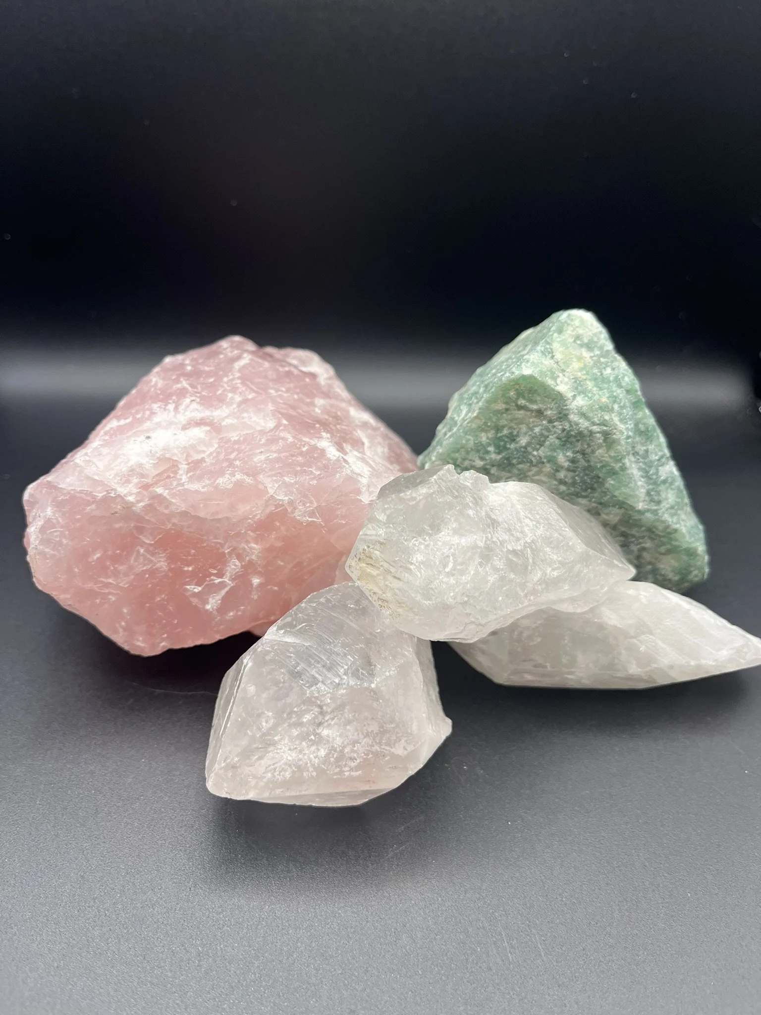 Group of colorful, rough, uncut gemstones in pink, green, white, and clear on a black background.
