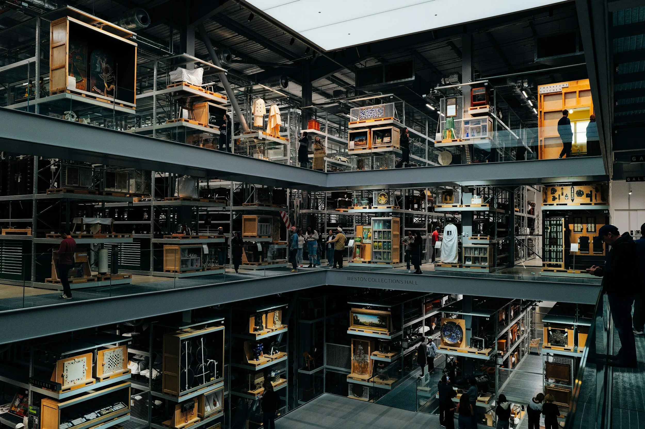 Multiple levels of storage shelves filled with various artwork, paintings, sculptures, and decorative items in a modern, industrial-style museum or gallery.