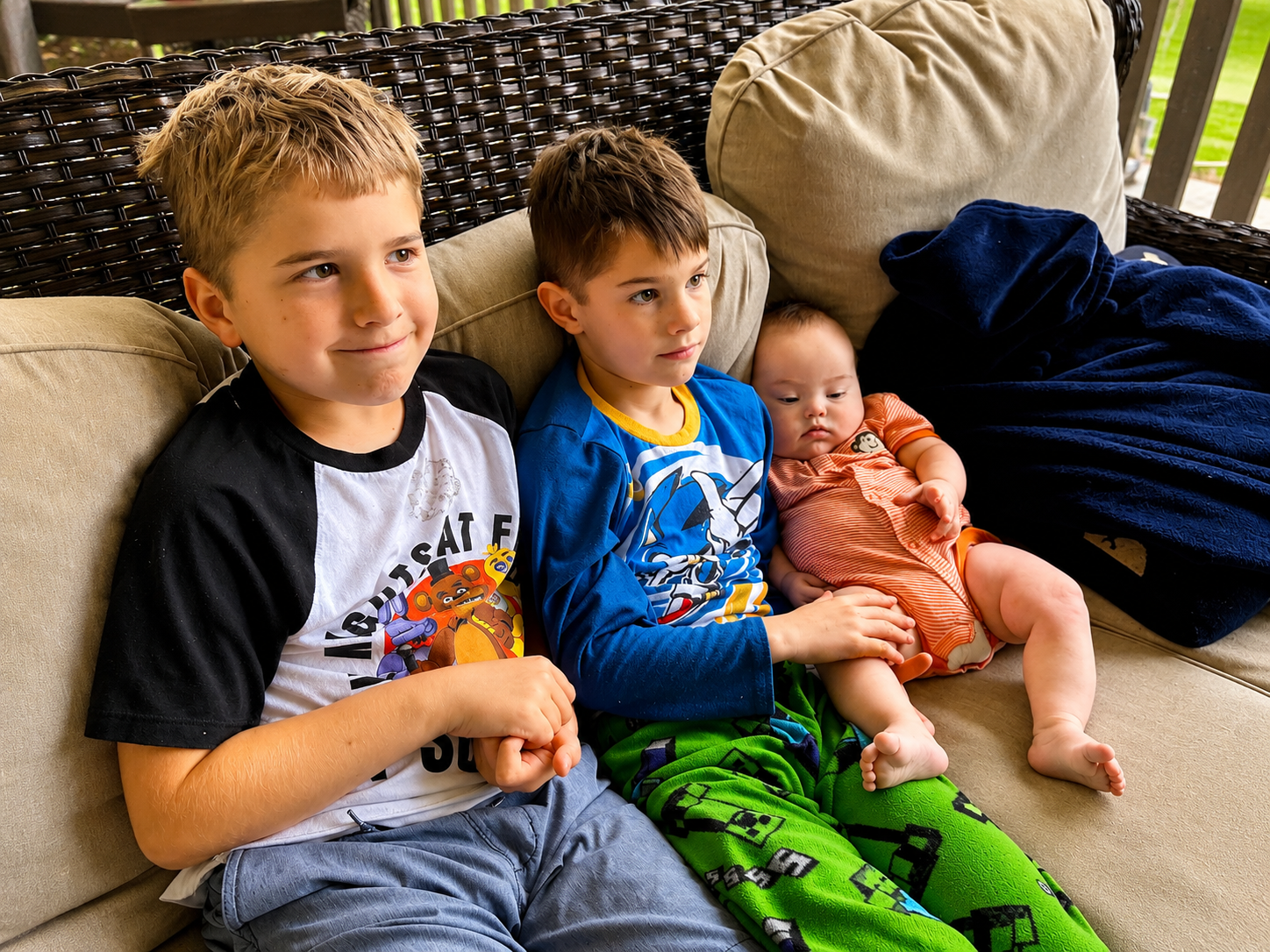 Cade, a baby with Down Syndrome being held by his two older brothers.