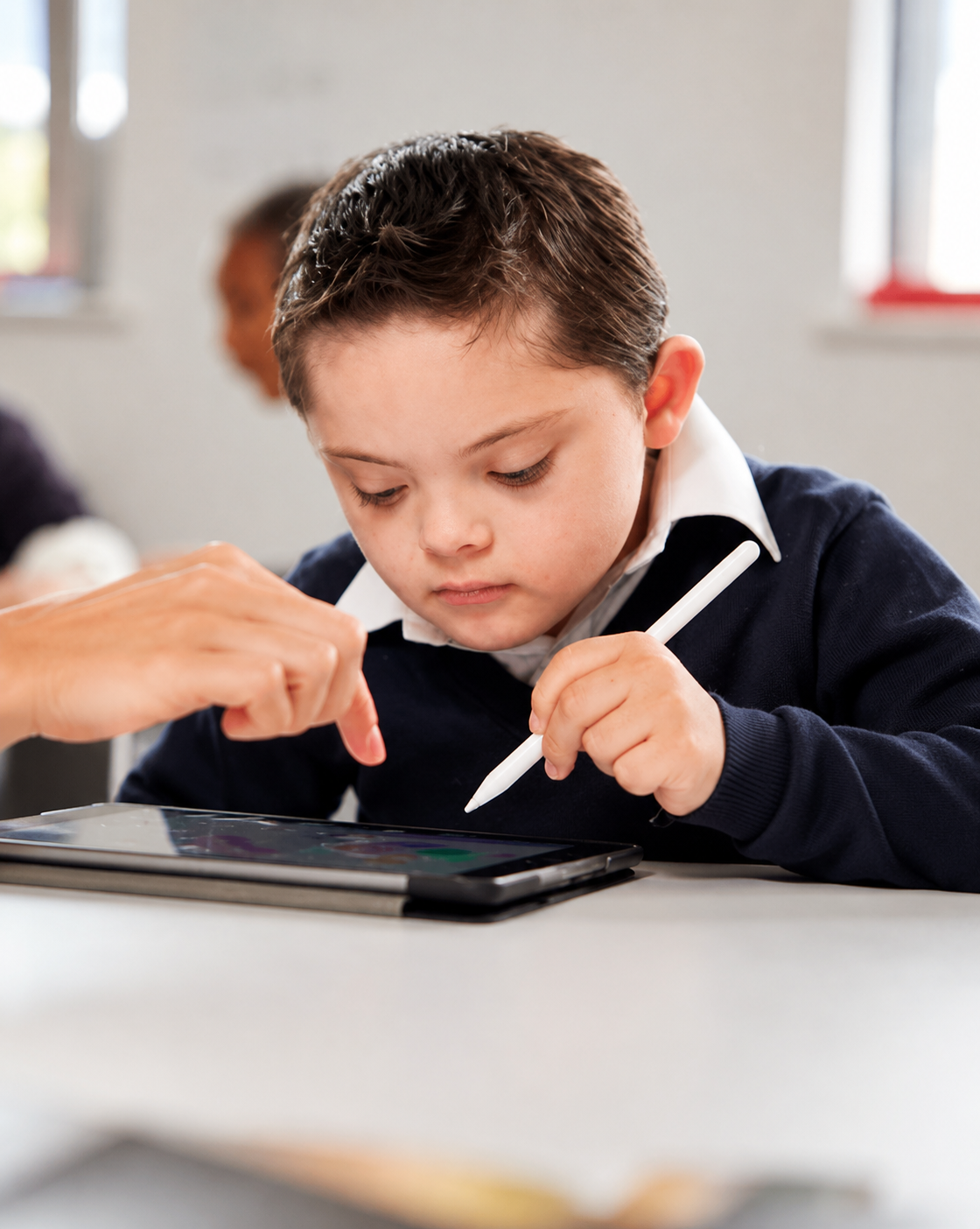 A young boy in a school uniform using a stylus on a tablet during class.